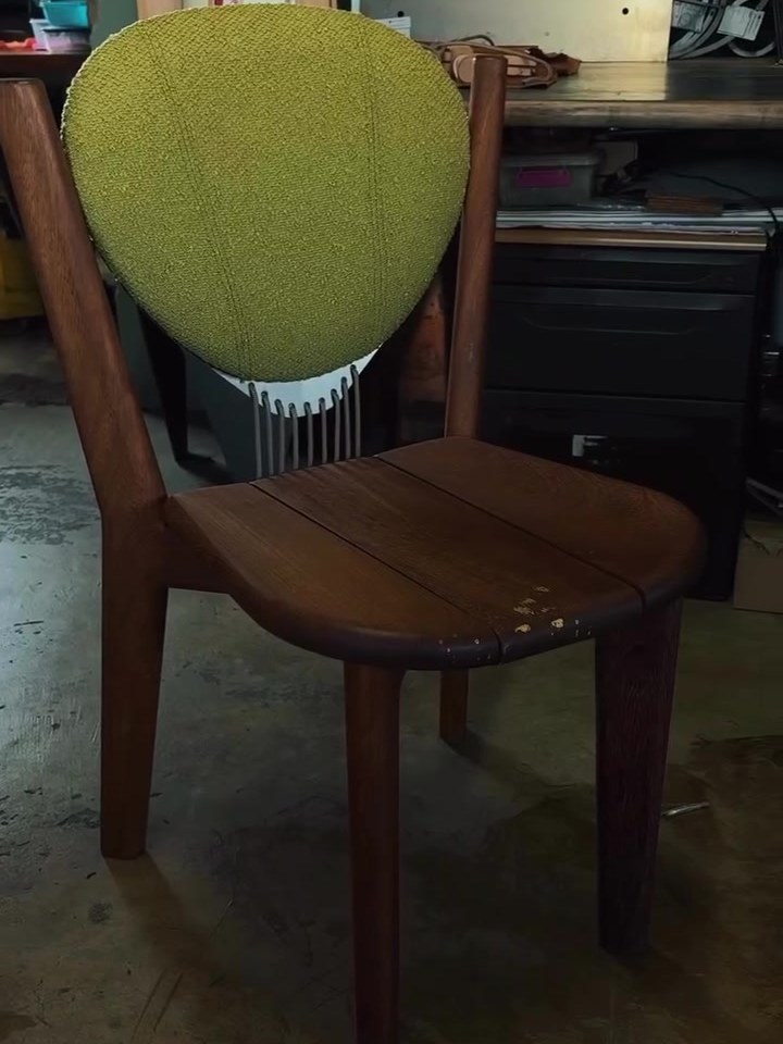 A timber dining chair with a green fabric back, made by the studio